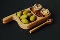 Large green olives with walnuts on unusual shaped beech tray and wooden spoon on black background