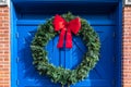 A large green outdoor Christmas holiday wreath with a bright red bow against a pair of bright cobalt blue doors Royalty Free Stock Photo