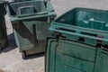 Large green trash cans, empty with lids open, curbside
