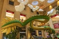 A large green and yellow dragon and a red and yellow bird and clouds hanging from the ceiling surrounded by lush green trees