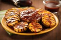 large grilled plantains with bbq sauce dripped over on a clay plate