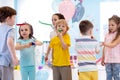 Large group of kids age 3 to 5 inside on a birthday party blowing noisemakers horns and twisted whistles