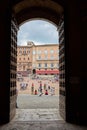 Large group of people in a public square seen from inside an arched doorway in Siena, Italy