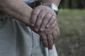 The large hands of an elderly man are folded on a cane with a watch on his right hand