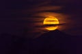 Large Harvest moon rising over Arizona mountains, partially covered by clouds