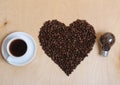 Large heart made of coffee beans, cup of coffee and bulb with coffee beans inside on a light wooden background, top view Royalty Free Stock Photo