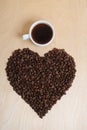 Large heart made of coffee beans and a cup of coffee on a light wooden background, top view Royalty Free Stock Photo