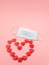 a large heart made of small red hearts and a medical mask on a soft pink background, copying the space. The concept of Royalty Free Stock Photo