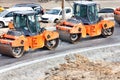 Large and heavy orange vibratory rollers compact the hot asphalt on the new road