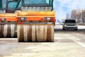 Large and heavy orange vibratory rollers move along the carriageway of the city road