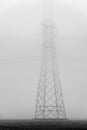 A large high voltage pylon is shrouded in the morning mist