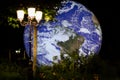 Large hologram of the planet earth at night with a street light and greenery in a park