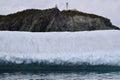 Large iceberg at the base of cliff in Twillingate Harbour with Long Point Lighthouse at the top Royalty Free Stock Photo