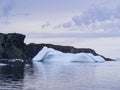 Large iceberg stranded next to sheer cliffs in Twillingate Harbour against cloud filled sky Royalty Free Stock Photo