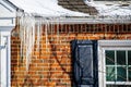 Large icicles hanging from snow covered roof of brick house indicating poor roof insulation Royalty Free Stock Photo