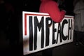 Large Impeach sign under the arm of person in red coat at night impeachment rally