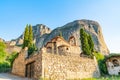 Large imposing rocks rise behind quaint Greek stone church