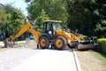 Large industrial backhoe loader parked across local road to prevent access to construction site surrounded with dense trees Royalty Free Stock Photo