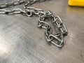 A large iron metal strong powerful shiny chain with links lies on an iron industrial table. Hand-held locksmith tools. The
