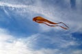 A large kite of yellow color tends upwards into the sky to white cirrus clouds