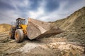A large loader or bulldozer digs hard into the rough terrain under an overcast sky, creating dust around its massive wheels Royalty Free Stock Photo