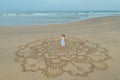 A large mandala painted on the sand on the ocean with a girl in the middle boho style.