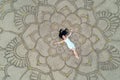 A large mandala painted on the sand on the ocean with a girl in the middle boho style.