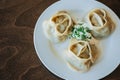 Large manti on a white dish with sour cream and herbs. Eastern cuisine. Meat in dough. Stands on a wooden table Royalty Free Stock Photo