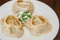 Large manti on a white dish with sour cream and herbs. Eastern cuisine. Meat in dough. Stands on a wooden table Royalty Free Stock Photo