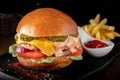 Large meal with cheeseburger with beef, cheese, tomatoes, cucumbers and French fries on a black wooden Board