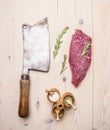 Large meat cleaver, with beef steak, rosemary and various spices wooden rustic background top view close up