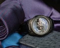 A large men`s watch against a pocket square, tie and ostrich leather wallets