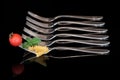 A large metal fork with pasta, basil and a tomato on it. In the background are empty forks in a row against a dark background Royalty Free Stock Photo