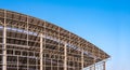 Large metal industrial factory building structure with steel curve roof and skylights in construction site against blue sky