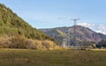 Large metal power pylon under electricity lines built in countryside with autumn grass and forest covered hills, blue sky Royalty Free Stock Photo