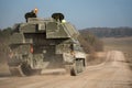 a large army tank driving down a dusty road in the country