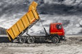 A large mining truck unloads the earth. A soil transporter with a raised body dumps soil. Contrast image against the sunset sky.