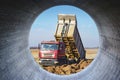 A large mining truck unloads the earth. A soil transporter with a raised body dumps soil. View through a large concrete pipe