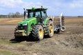 A large modern John Deere tractor tows a cultivator in a field