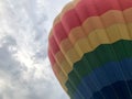 Large multi-colored bright round rainbow colored striped striped flying balloon with a basket against the sky in the evening Royalty Free Stock Photo