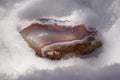 Large multi-colored layered piece agate chalcedony gem in the sunlight on the snow winter background close-up