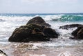 Large multi-layered boulders on beach with ocean waves hitting it as they approach the shore. Royalty Free Stock Photo