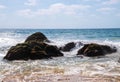 Large multi-layered boulders on beach with ocean waves hitting it as they approach the shore. Royalty Free Stock Photo