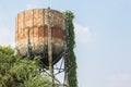 Large old iron water tank tower full of rust and covered trees  on blue sky background Royalty Free Stock Photo