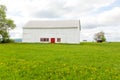 Large old wooden white barn with red door and window trim set in a grassy field Royalty Free Stock Photo