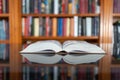 Large open book on top of a glass table with a library full of books in the background. Royalty Free Stock Photo