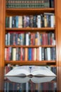 Large open book on top of a glass table with a library full of books in the background. Royalty Free Stock Photo