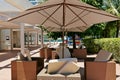 A large open clear parasol. Several empty pool chairs. In the background, deck and vegetation.