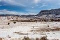 Large open snow covered field with vintage barbwire fence in front of a large mesa plateau with clouds in sky