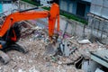 A large orange backhoe uses its forearms to sweep and scoop up rubble. at the construction site